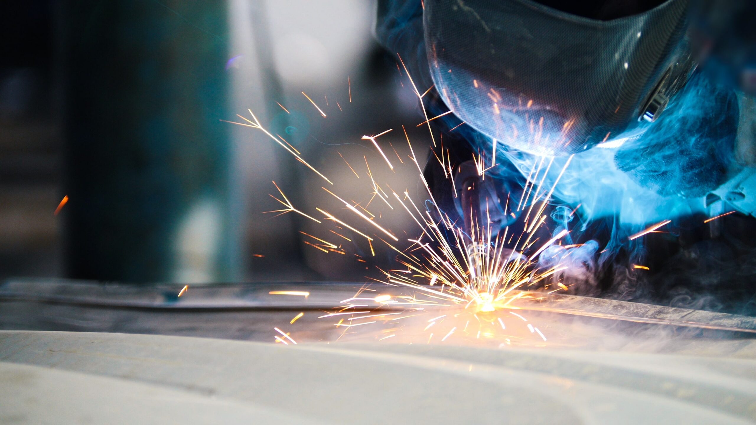 Employee welding steel while wearing safety gear, sparks flying