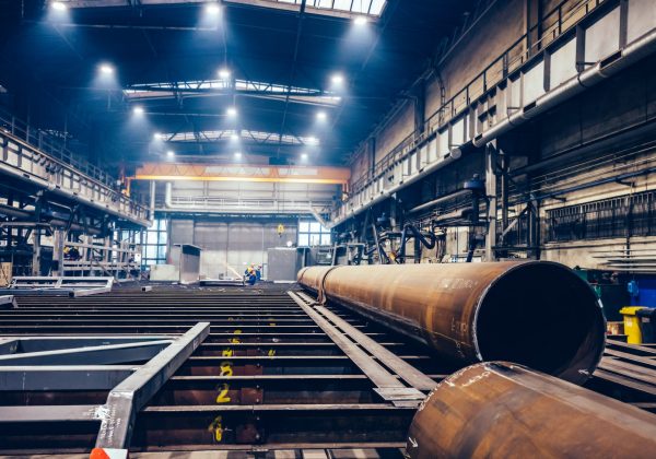 pipes-and-steel-profiles-in-a-big-factory-shipyar-2022-12-16-11-05-53-utc-min.jpg Pipe in the manufacturing process in the factory with employees in the distant