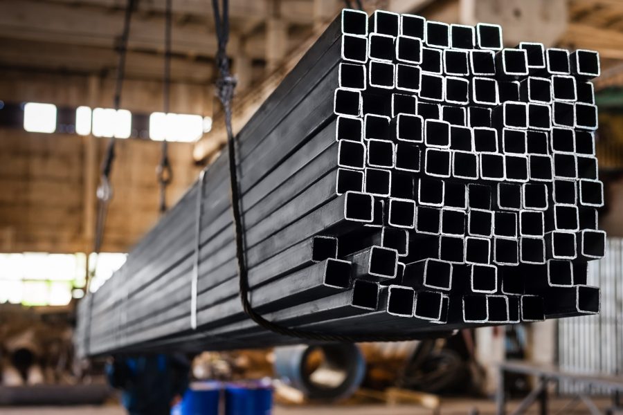 Square pipes stacked and in the process of being transported by metal cords on lift